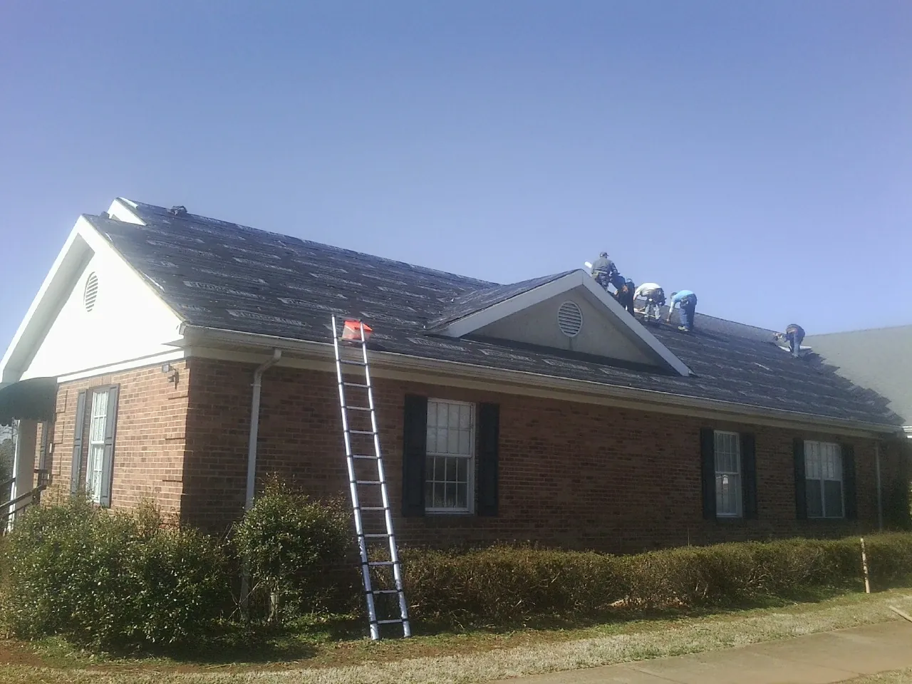 Crew tearing shingles off a brick ranch roof with a ladder set — Emergency Roof Repair work by our crew in Llano